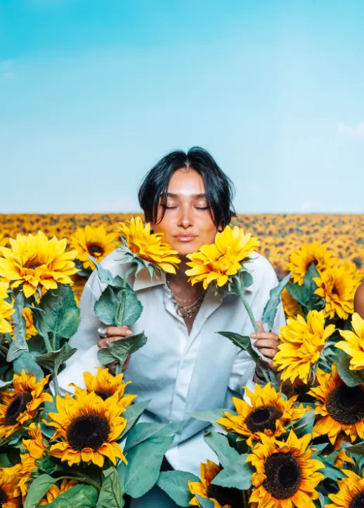 Eine Frau steht in einem Sonnenblumenfeld und genießt die sonnige Atmosphäre und die blühenden Blumen um sie herum.