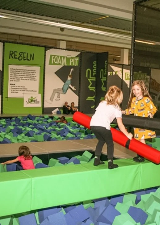 Zwei Kinder springen fröhlich auf einem Trampolin in einem Indoor-Spielbereich.