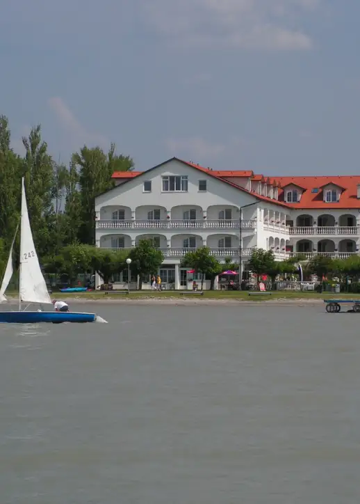 Großes, elegantes weißes Gebäude des Seehotels Herlinde, umgeben von malerischer Landschaft und glitzerndem Wasser.