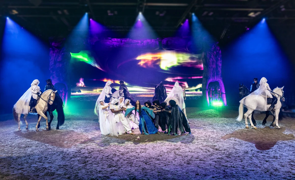 Eine Gruppe von Menschen in Kostümen steht auf der Bühne, umgeben von prächtigen Pferden während der CAVALLUNA-Show.