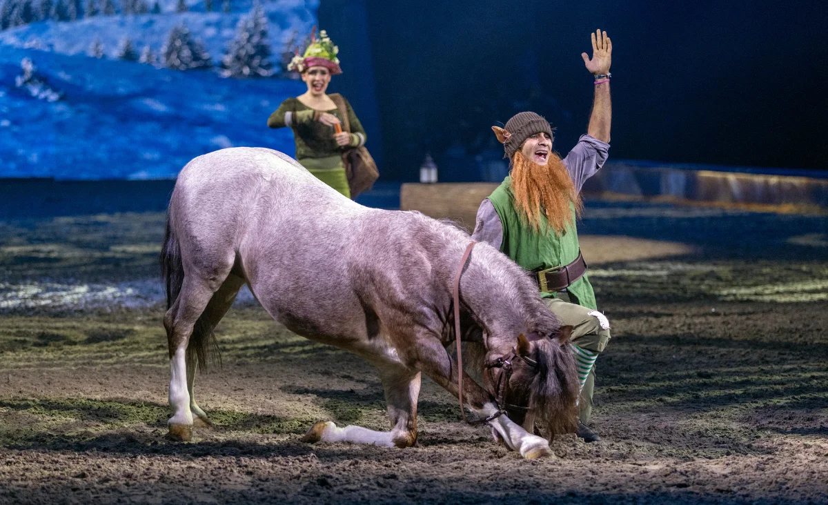 Ein Mann im grünen Kostüm streichelt ein Pferd während der CAVALLUNA-Show in Berlin, die magische Abenteuer erzählt.