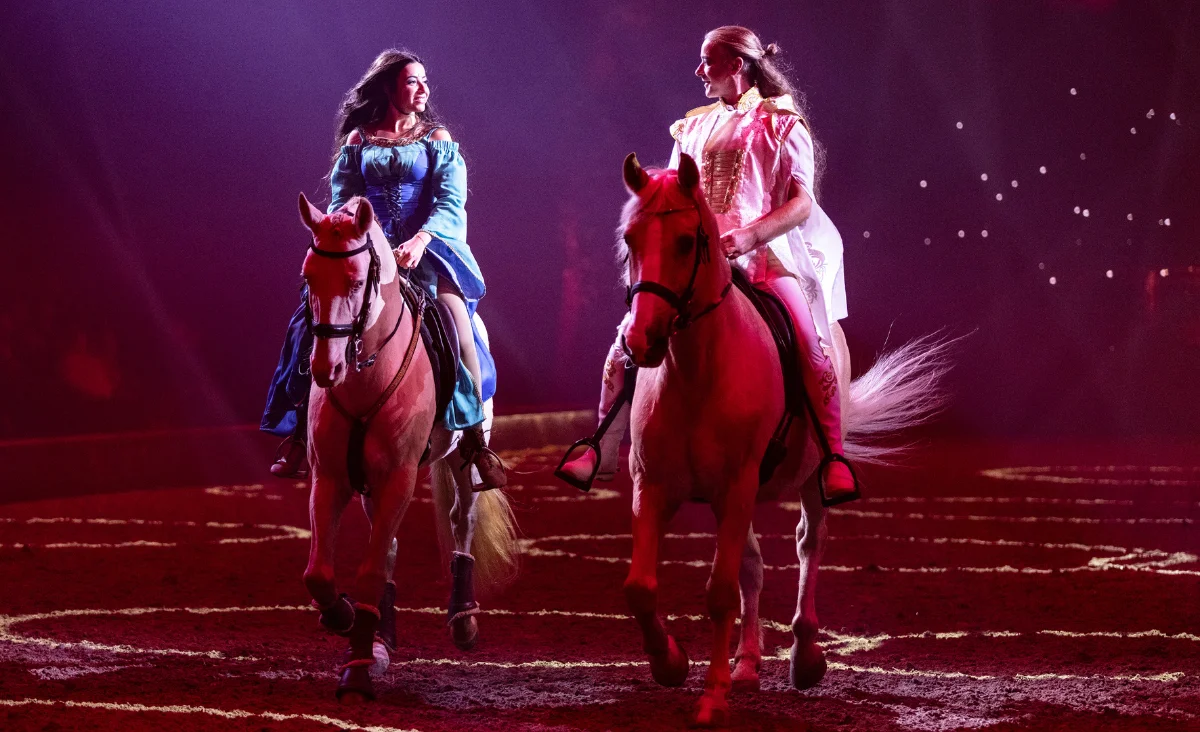Zwei Frauen in Kostümen reiten auf Pferden in einer Arena während der CAVALLUNA-Show in Berlin.