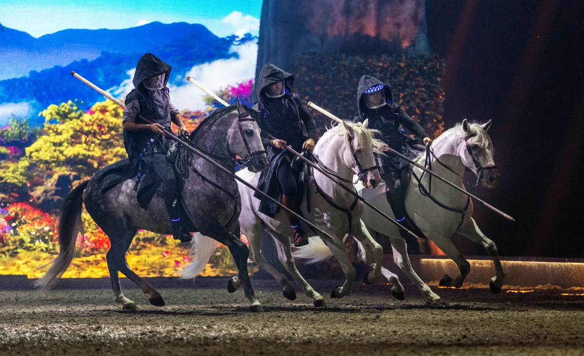 Eine Gruppe von Menschen reitet auf Pferden in einem Ring während der CAVALLUNA-Show in Berlin.