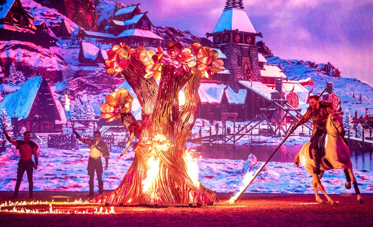 Ein Mann auf einem Pferd hält eine Fackel vor einem Feuer, das die mystische Atmosphäre der Show CAVALLUNA unterstreicht.