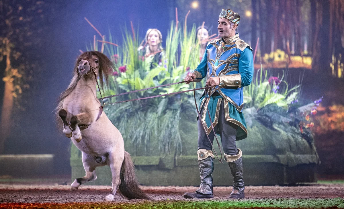 Ein Mann in einem Kostüm hält ein Pferd, das Teil der CAVALLUNA-Show in Berlin ist, die magische Welten präsentiert.