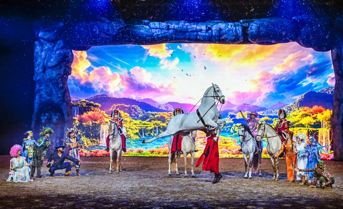 Eine Gruppe von Menschen auf Pferden steht vor einer großen Leinwand, die für die CAVALLUNA-Show in Berlin wirbt.