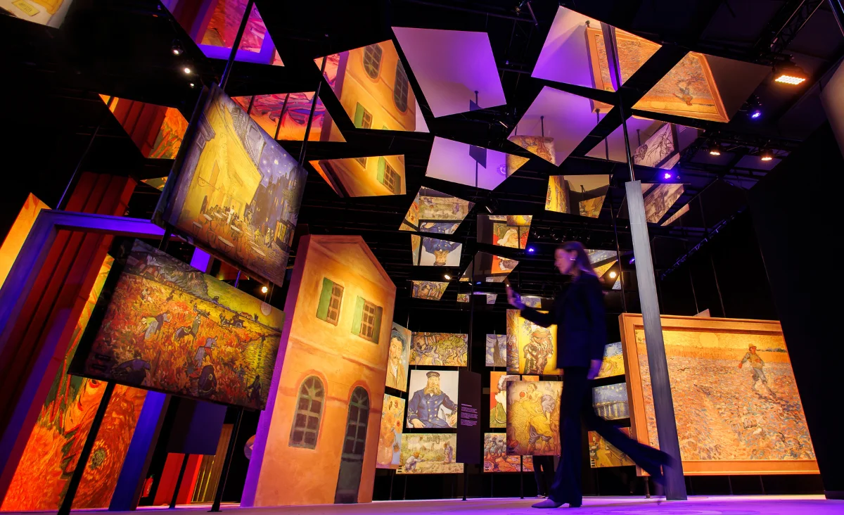 Eine Frau geht durch einen Raum voller Gemälde bei der Van Gogh immersiven Ausstellung.