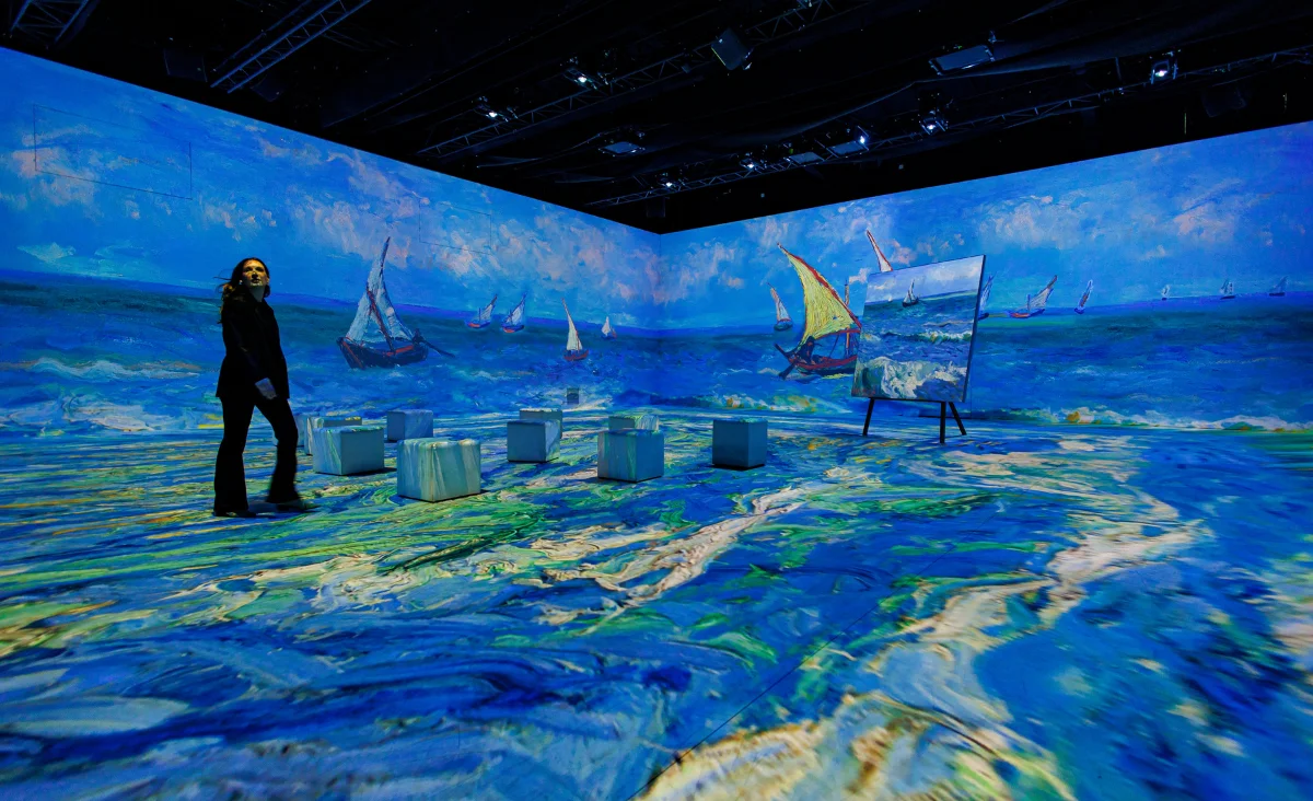 Eine Frau steht vor einem Kunstwerk in der Van Gogh immersiven Ausstellung.
