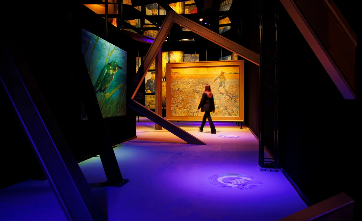 Eine Frau geht durch einen dunklen Raum in der Van Gogh immersiven Ausstellung.