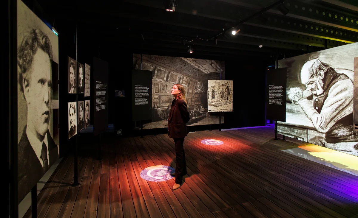 Eine Frau steht vor einer Fotogalerie in der Van Gogh immersiven Ausstellung.