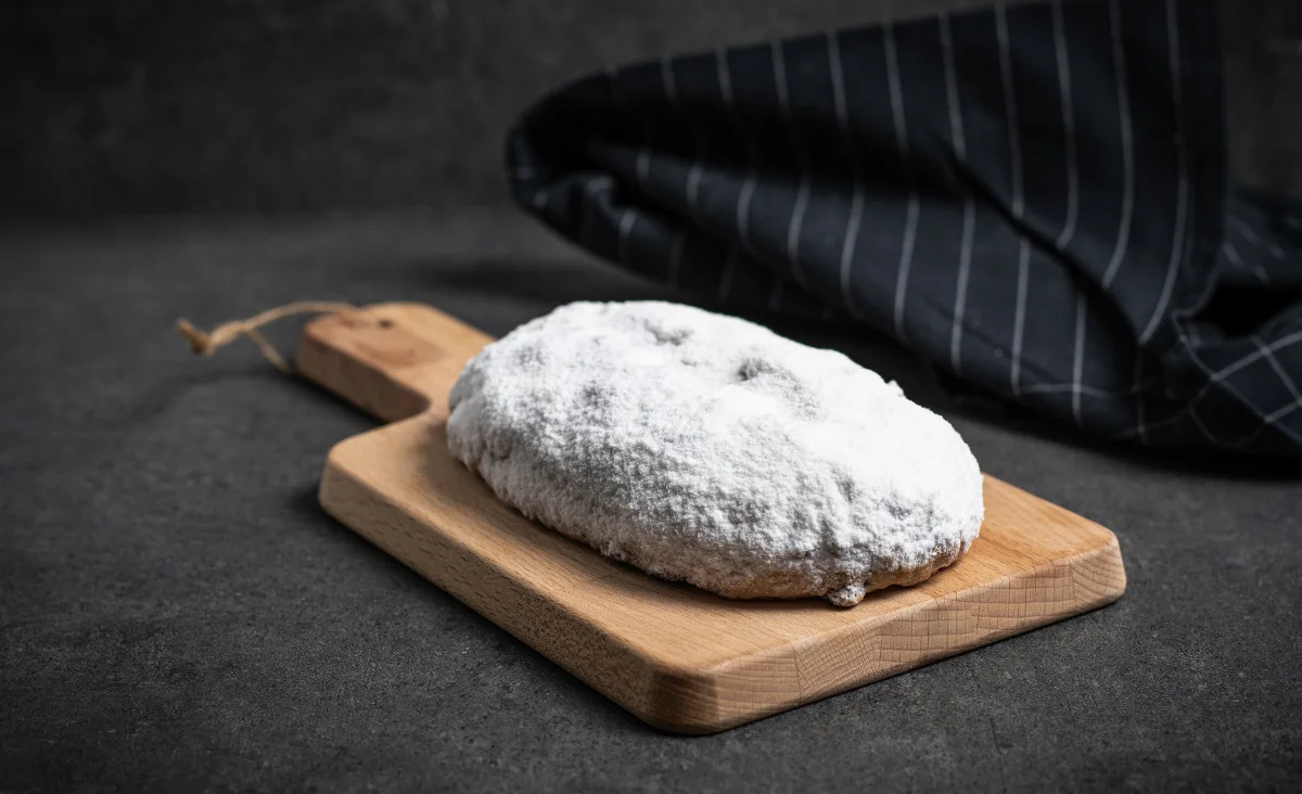 Ein frisch gebackener Dresdner Christstollen mit Rosinen und Nüssen auf einem Holzbrett, hergestellt von Stollenbäckerei Krause.