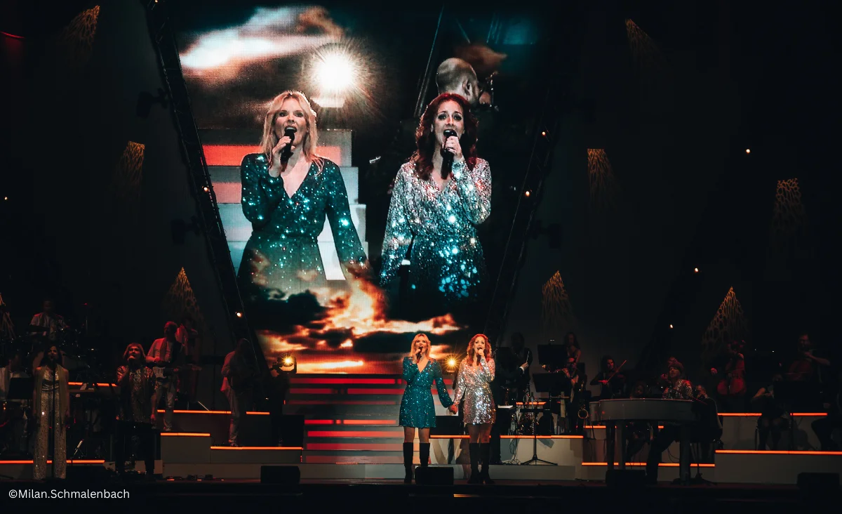 Zwei Frauen auf der Bühne mit einem großen Bildschirm im Hintergrund während ABBAMANIA THE SHOW in Berlin am 18.04.2026.