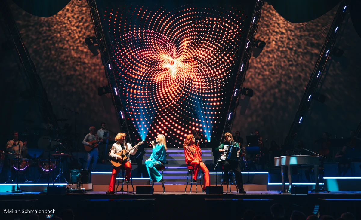 Auf der Bühne stehen mehrere Personen vor einem großen Bühnenhintergrund während der ABBAMANIA THE SHOW in Berlin.