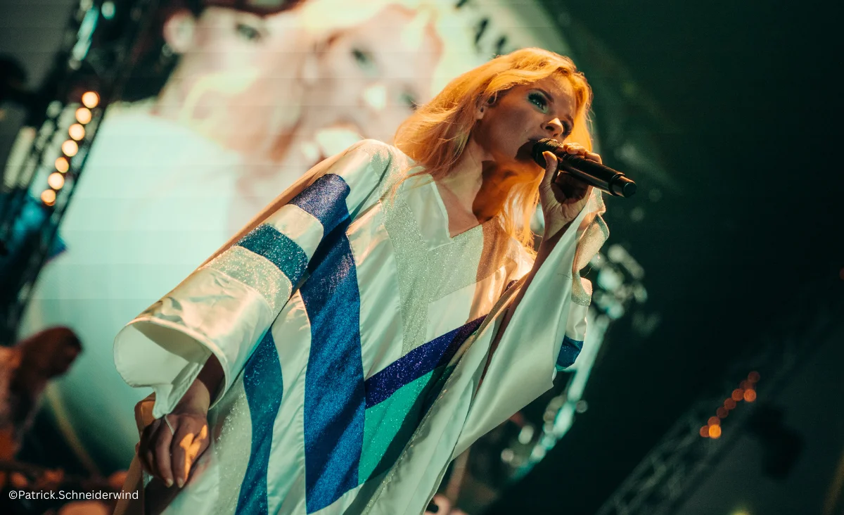 Eine Sängerin in einem weißen Robe, die ins Mikrofon singt, bei ABBAMANIA THE SHOW in der Uber Arena, Berlin, am 18.04.2026.