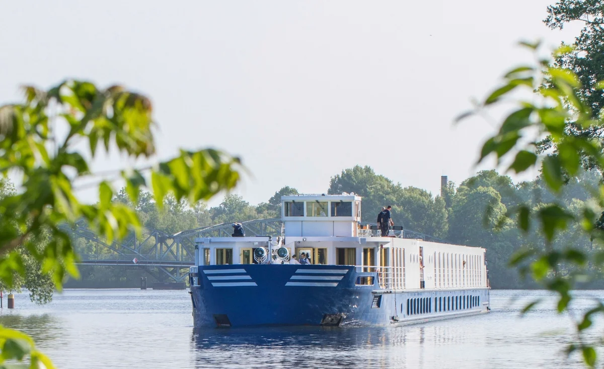 Ein großes blau-weißes Boot-MS Thurgau Chopin - fährt gemächlich einen Fluss entlang, ideal für eine 8-tägige Flusskreuzfahrt für zwei.
