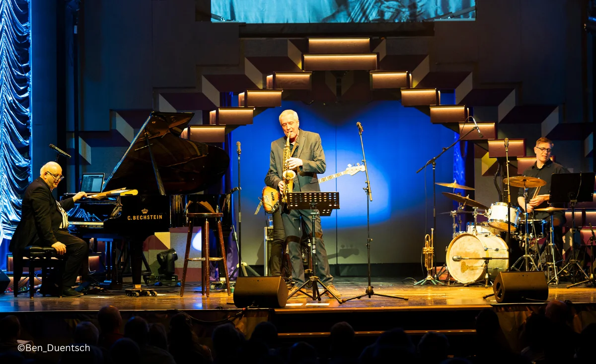 Ein Mann spielt Saxophon und tritt mit seiner Band gemeinsam auf der Bühne auf.