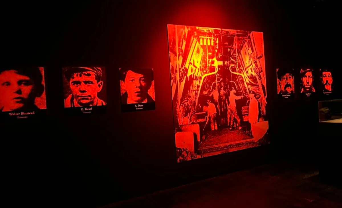 Rotes Licht beleuchtet eine Wand mit Bildern von Menschen aus der Titanic-Ausstellung.