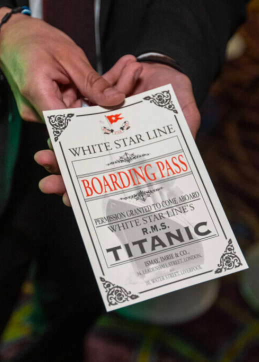 Hand hält einen Boarding-Pass der White Star Line für das Schiff R.M.S. Titanic mit dekorativem Rahmen und rotem Schriftzug