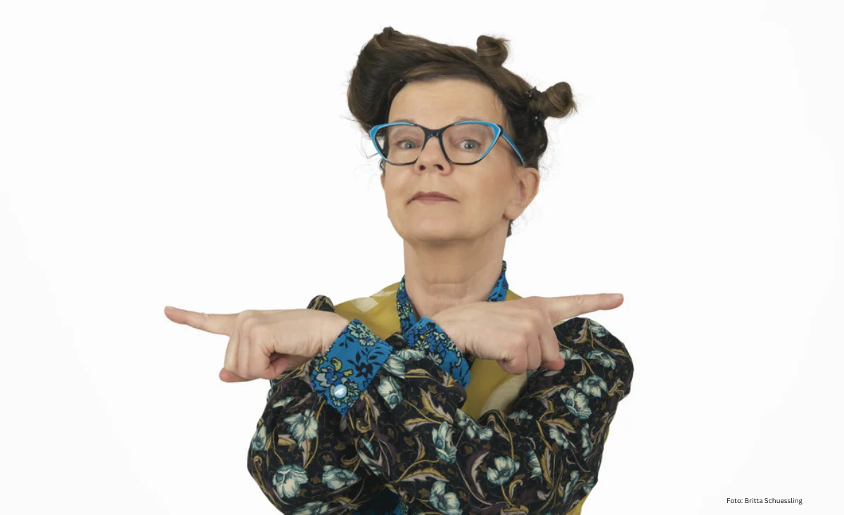 Eine Frau mit hochgestecktem Haar und gemustertem Oberteil zeigt mit beiden Händen nach rechts