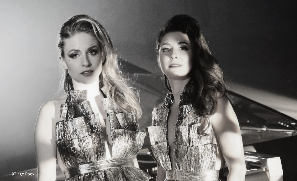 Queenz of Piano Duo in glänzenden Bühnenoutfits vor einem Konzertflügel