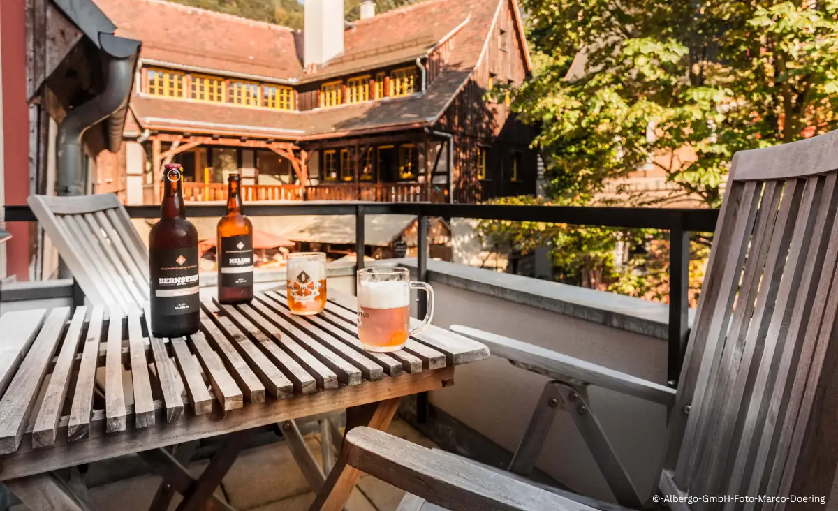 Balkon mit Holztisch und zwei Stühlen vor dem Hotel Zur Mühle in Schmilka, auf dem Tisch stehen zwei Bierflaschen, ein Bierglas und ein Glas mit Getränk.
